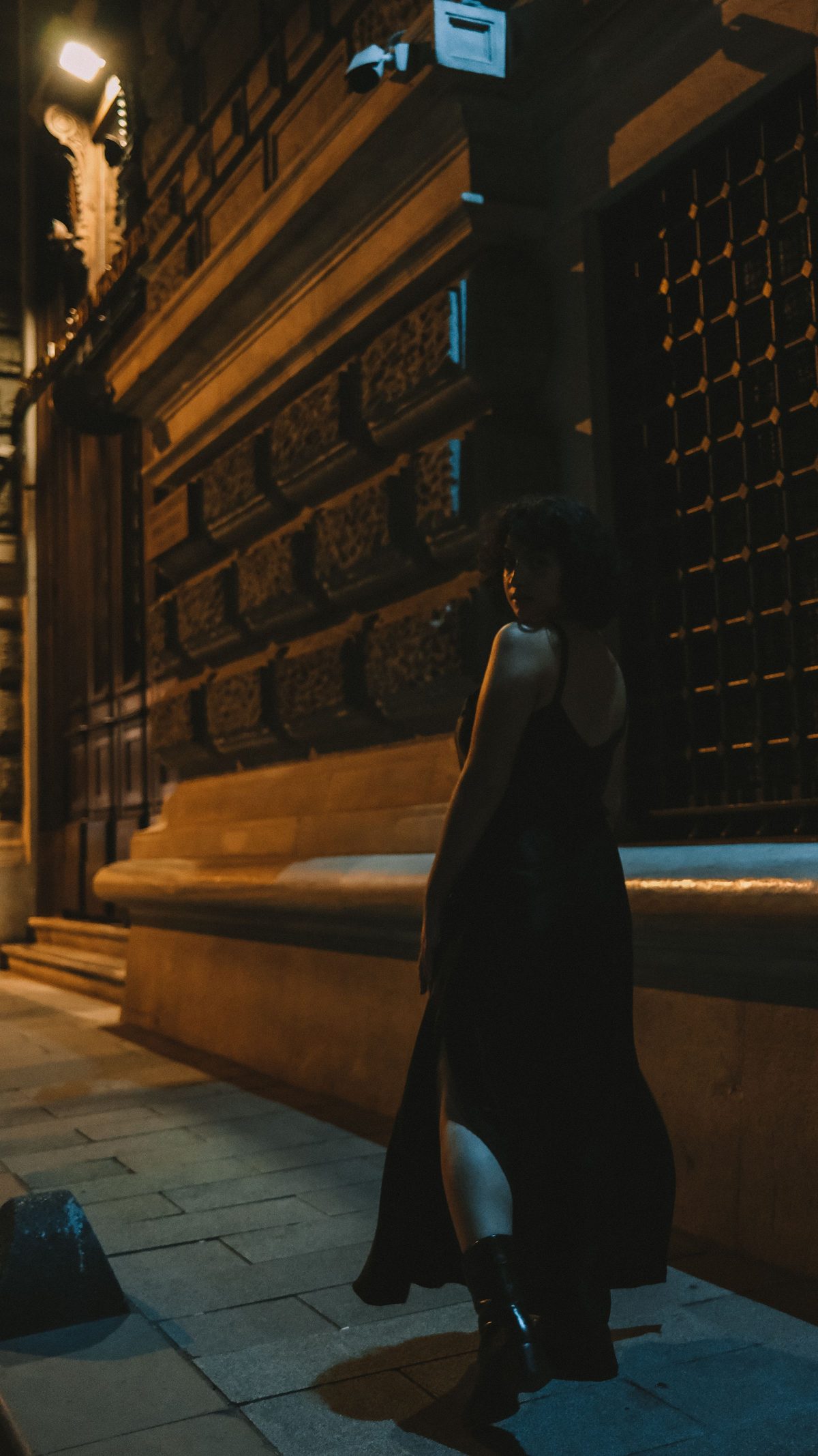 A woman in a black dress on a city street at night
